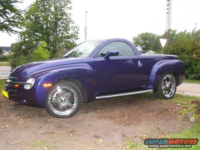 Purple 2004 Chevrolet SSR parked on dirt with trees and houses in background