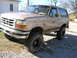 1996 Ford Bronco - A mud-covered Ford Bronco sits on a gravel lot, its body and tires caked with dirt.