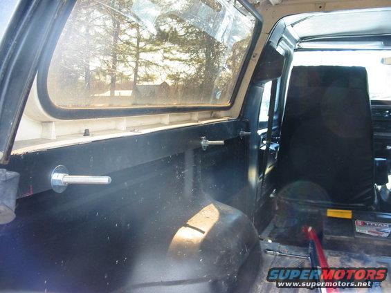 Interior of a vehicle with black seats and metal mounting bolts visible on the side panel