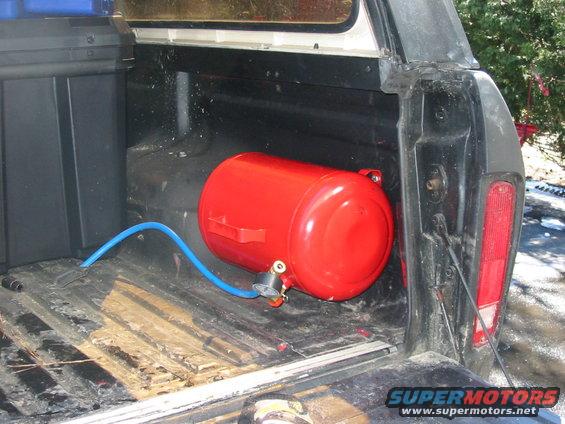 Red air tank and blue hose in the bed of a pickup truck next to a black storage box