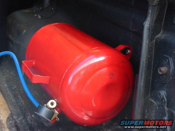 Red cylindrical air tank with blue hose and pressure gauge, mounted inside a dark vehicle