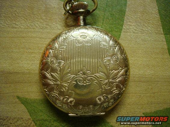 Gold pocket watch with floral engraving, top loop visible, on a patterned surface
