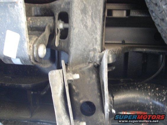 Undercarriage of a vehicle showing metal brackets and bolts, with a tire visible on the right