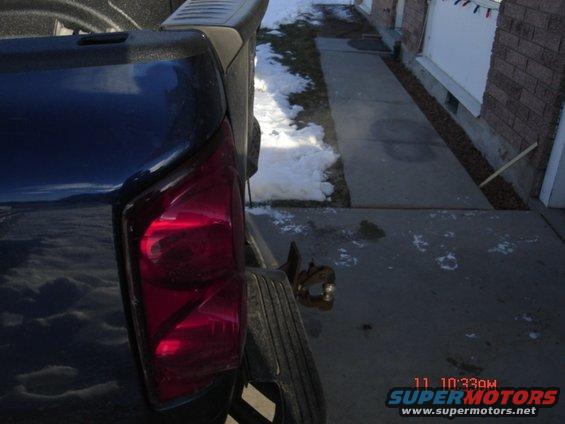 Pickup truck's red taillight and spare tire mounted on the rear bumper. Snow is on the ground next to a concrete walkway