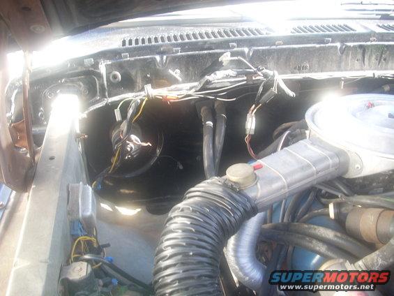 Engine bay with hoses, wires, and air intake visible. Some text on a watermark is present