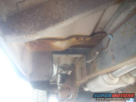 Undercarriage of a truck showing frame, exhaust, and suspension components. Some rust is visible