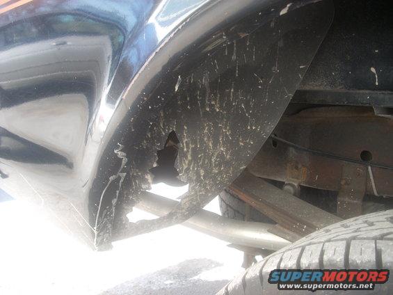 Damaged rear wheel well liner and suspension components on a dark vehicle
