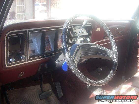 Car interior dashboard with maroon trim, a cracked steering wheel cover, and a "SUPERMOTORS" watermark