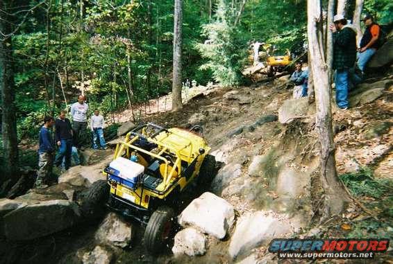 Yellow off-road vehicle with roll cage navigating rocky terrain, cooler strapped to rear