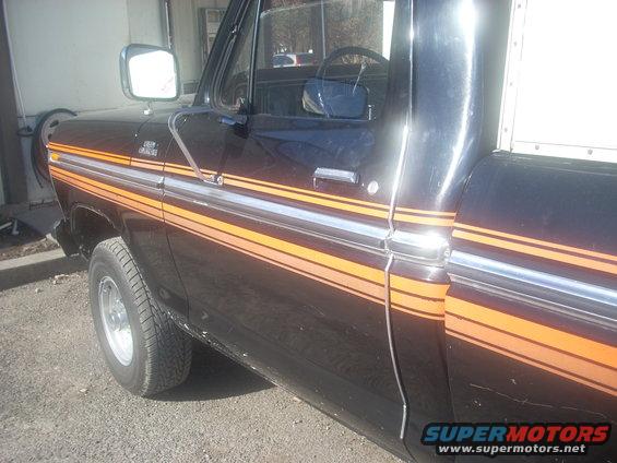 Dark brown 1970s Ford F-Series truck with orange and silver side stripes, viewed from the side