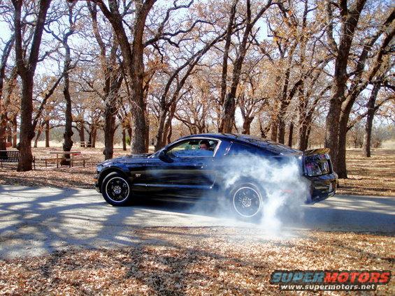 Dark blue Ford Mustang doing a burnout, rear-wheel drive, with smoke billowing