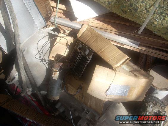 Dashboard vents and a motor are piled with boxes and scrap wood