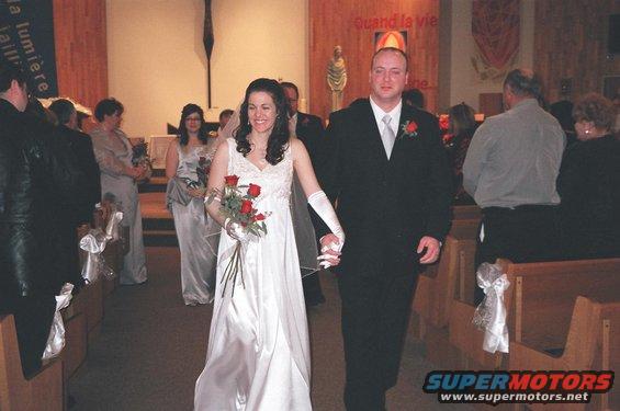 Bride and groom walking down church aisle, wedding party behind them
