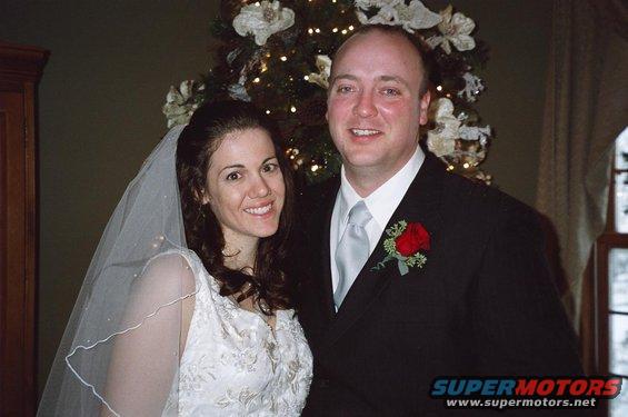 Bride and groom in wedding attire posing in front of a decorated Christmas tree