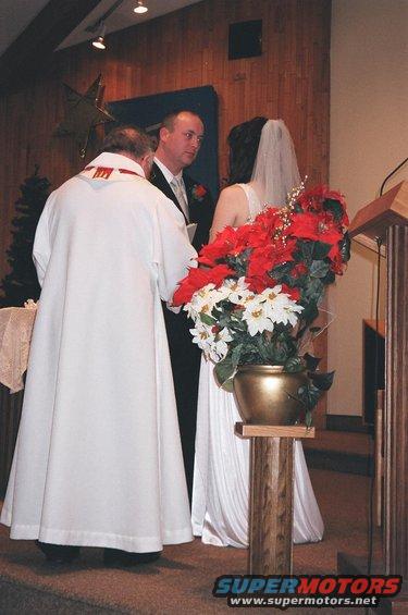 Wedding ceremony with officiant, groom, and bride. Potted poinsettias are in the foreground
