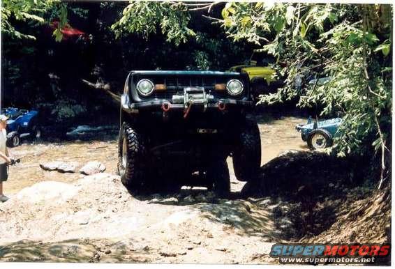 Modified off-road vehicle with winch on rocky terrain. Another ATV and yellow vehicle visible in background