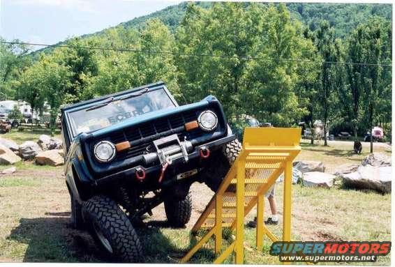 Blue 1976 Ford Bronco on a dirt incline with a yellow ramp, front winch visible