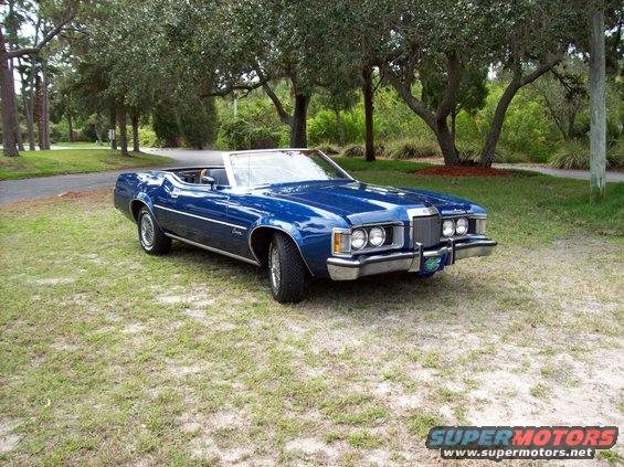 Blue 1973 Mercury Cougar convertible parked on grass with trees in background