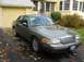 2001 Ford Crown Victoria - Gray 2001 Ford Crown Victoria parked in front of a yellow garage on an autumn day.