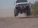 1992 Ford Bronco - This lifted SUV is airborne over a dirt track, kicking up dust.