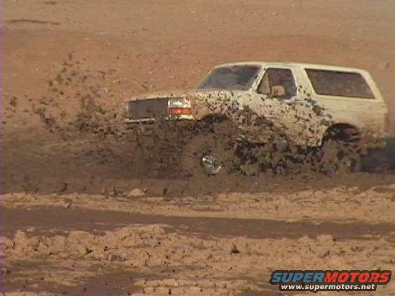 White 1992 Ford Bronco stuck in mud, splashing dirt
