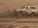 1992 Ford Bronco - White 1992 Ford Bronco driving through a muddy area, kicking up a lot of dirt.