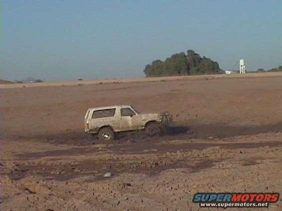 White SUV stuck in mud, side view, clear sky, dry terrain