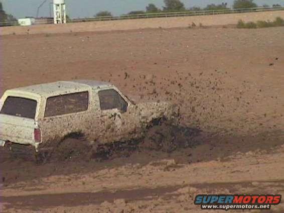 White SUV with mud splashing up its sides, stuck in a muddy field