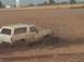 1992 Ford Bronco - A white SUV is stuck in a mud pit, with mud spraying from its wheels.
