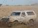 1992 Ford Bronco - Ford Bronco is stuck in the mud, with mud flying everywhere.