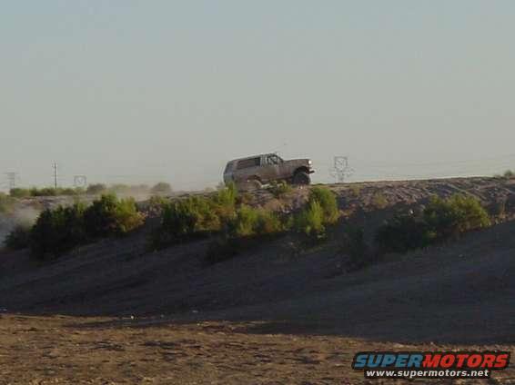 Tan 1992 Ford Bronco driving on a dirt hill, kicking up dust