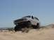 1992 Ford Bronco - A white 1992 Ford Bronco navigates sandy terrain under a clear blue sky.