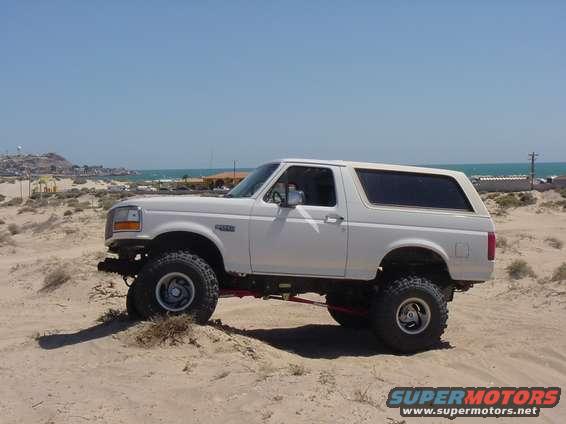 White 1992 Ford Bronco parked on a sand dune with the ocean in the background