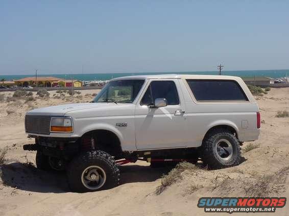 White 1992 Ford Bronco parked on sand with ocean in background
