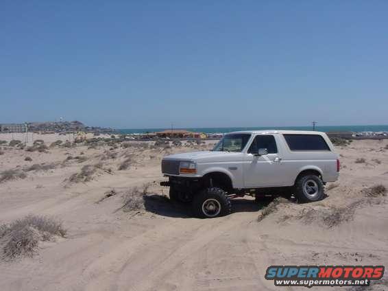 White Ford Bronco parked on sand dunes near the ocean