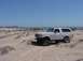 1992 Ford Bronco - A white Ford Bronco is parked on a sandy terrain with the ocean in the background.