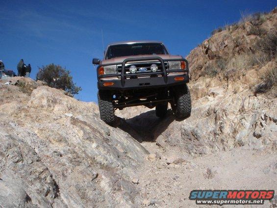 Brown 1987 Ford Bronco off-roading on a rocky incline, front view with bull bar