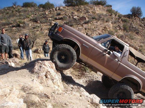 Brown 1989 Ford Bronco climbing a steep, rocky hill with people watching