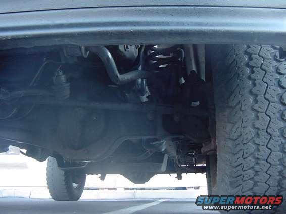 Underside view of a truck's suspension and drivetrain components, with a tire visible on the right