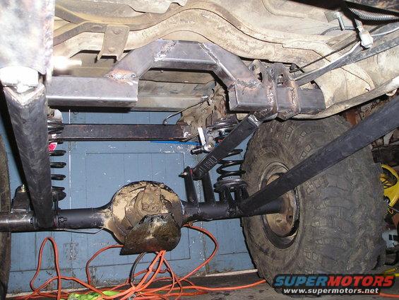 Underside of a vehicle showing a custom-welded suspension setup with a large tire and differential