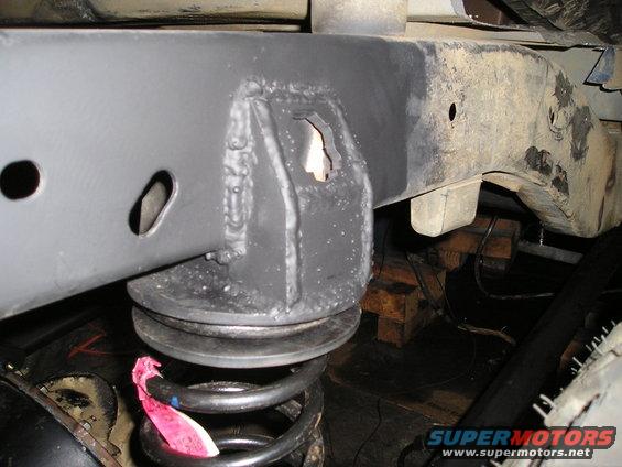 Vehicle frame with suspension spring and mounting bracket, gray paint, some rust visible