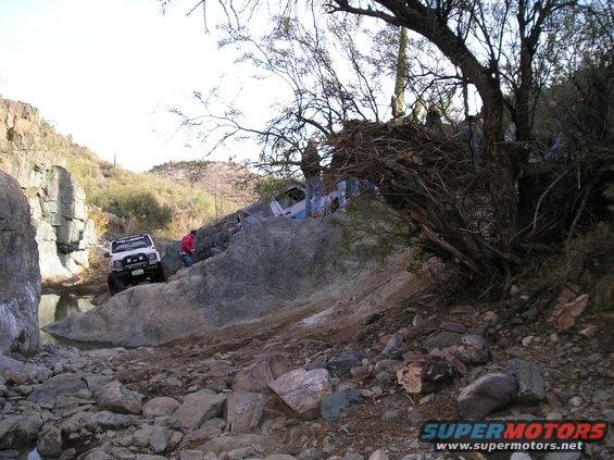White off-road vehicle on rocky terrain with another vehicle partially visible up a slope