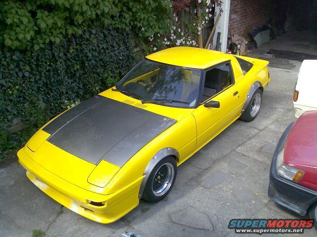 Yellow 1983 Mazda RX-7 with wide fender flares and a matte black hood