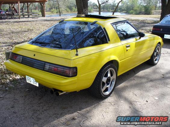 Yellow 1983 Mazda RX-7 parked outdoors near trees and water