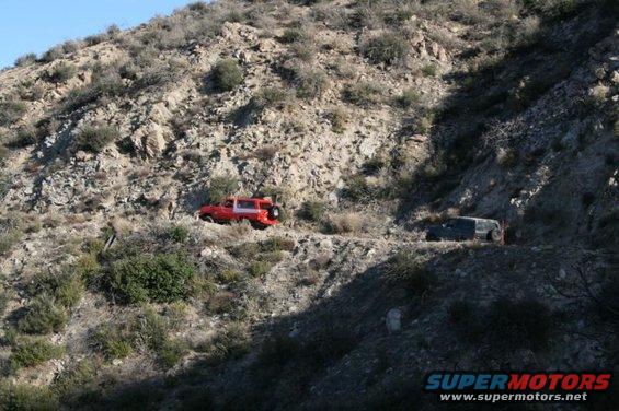 Red and dark SUVs driving on a rocky, mountainous dirt road