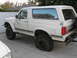 1990 Ford Bronco - White 1990 Ford Bronco parked on a concrete driveway, showing off-road modifications and a flat rear tire.