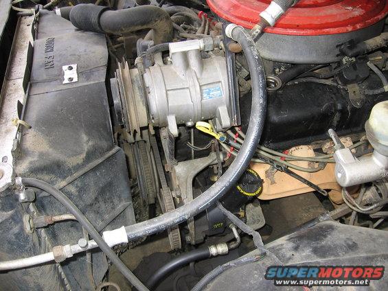 Engine compartment with AC compressor, radiator fan shroud, and hoses visible