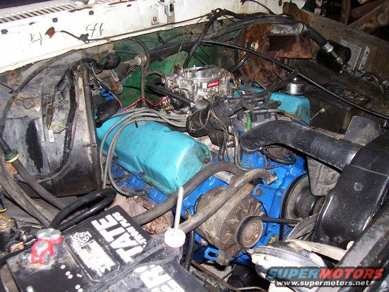 Engine bay with blue valve covers, a carburetor, and a battery