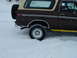 1979 Ford Bronco - Brown 1978 Ford Bronco with tan top driving through snow, spare tire visible on rear.
