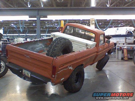 Orange pickup truck with a spare tire and toolbox in the bed, viewed from the rear three-quarter angle